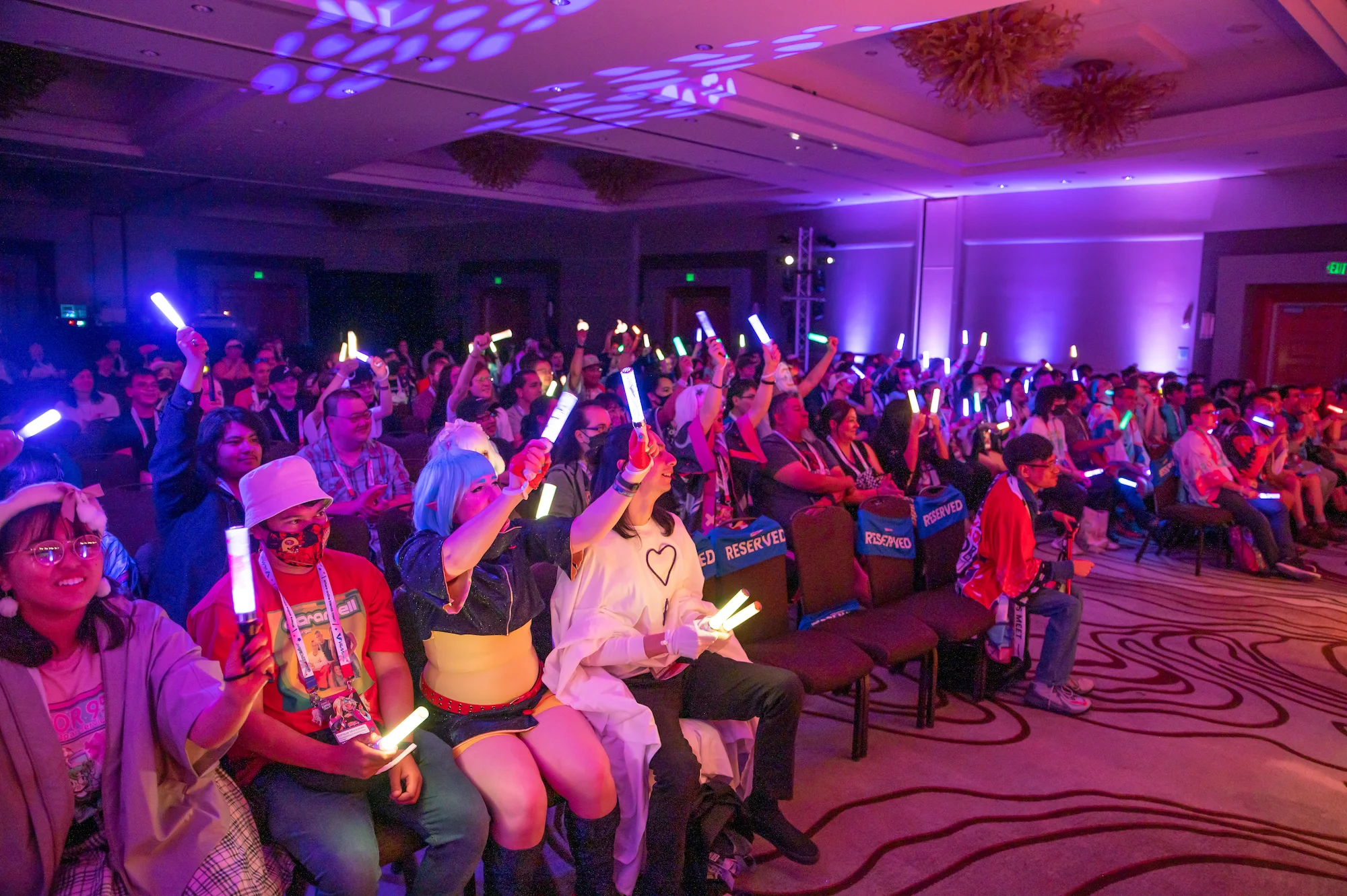 Audience at a live event with glowing penlights in purple stage lighting