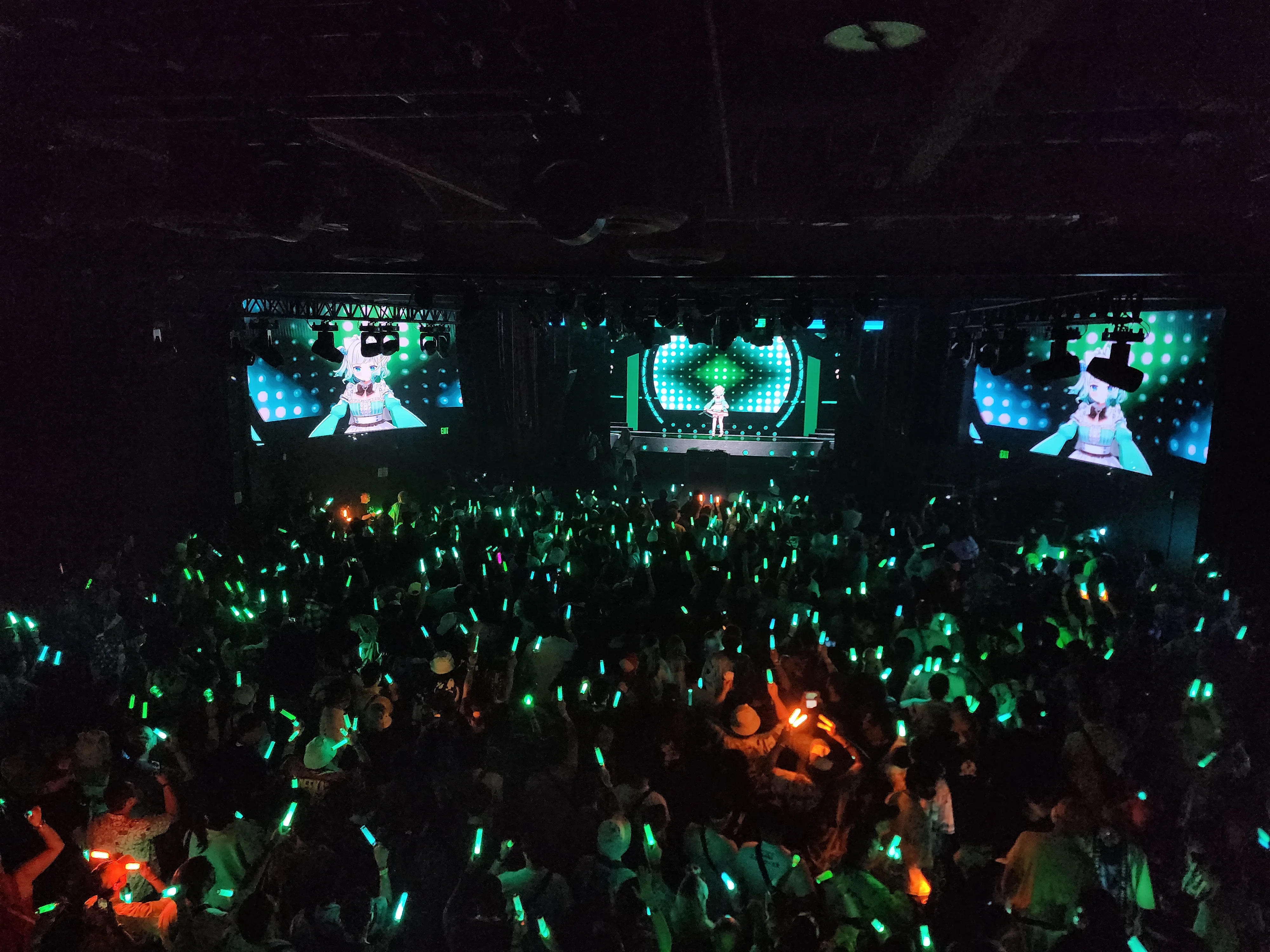 Live concert with VTuber stage screens and crowd holding green penlights