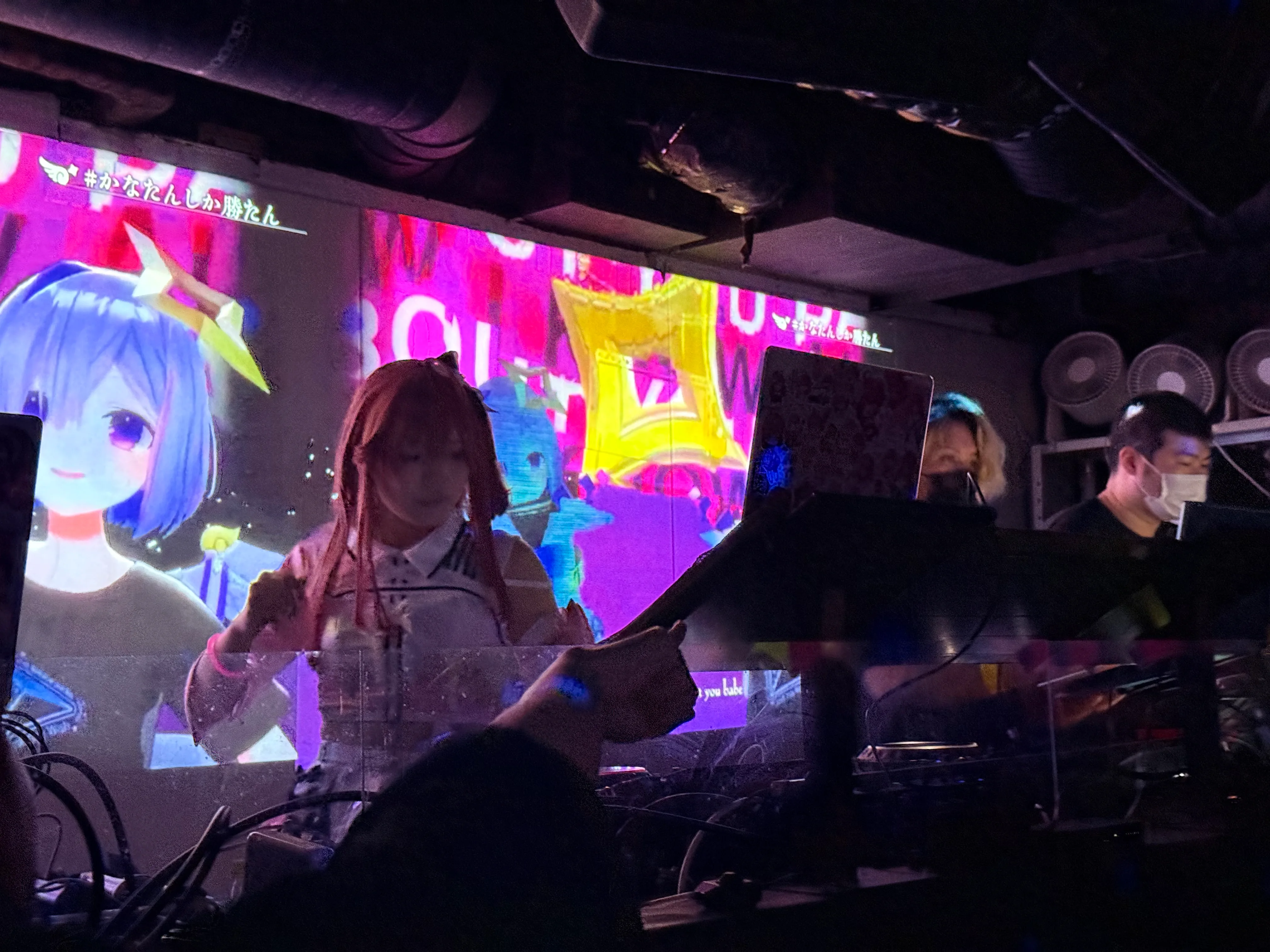 DJ performance at MOGRA with laptops and a large screen showing colorful VTuber-style visuals